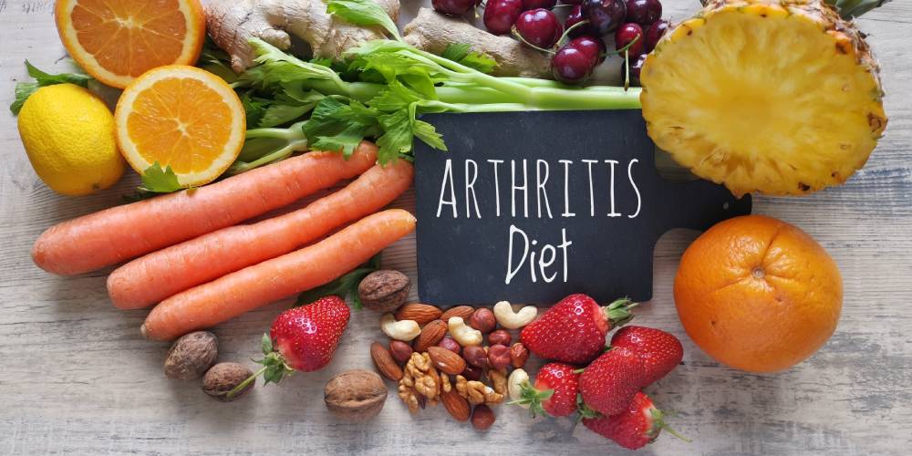 The term "arthritis diet" written in white on a black chart, placed in the middle of healthy fruits, vegetables and nuts arranged on a white wooden table.